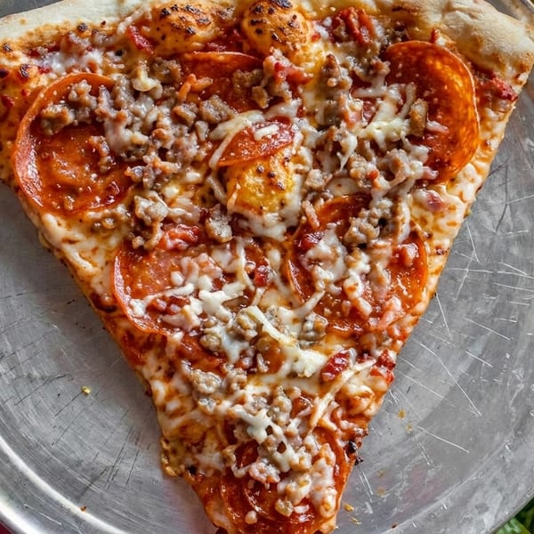 A large slice of pepperoni and sausage pizza on a metal tray, with lettuce and pickles.